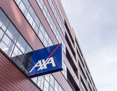 Ein modernes Bürogebäude mit roten Ziegeln und grossen Fenstern, an dem ein blaues AXA-Logo mit weisser Schrift und rotem Streifen angebracht ist.