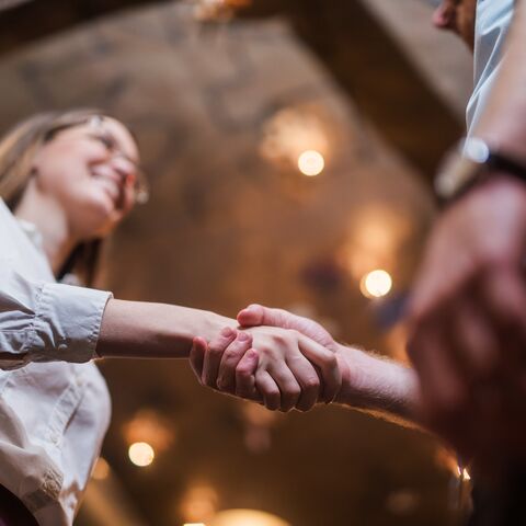 Two people shake hands in a warmly lit room. The scene appears friendly and professional.