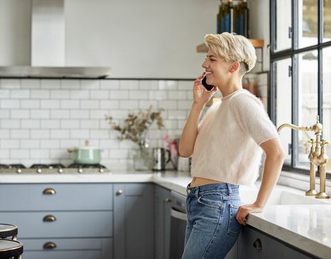 Eine junge blonde Frau ist zu Hause in der Küche und telefoniert.