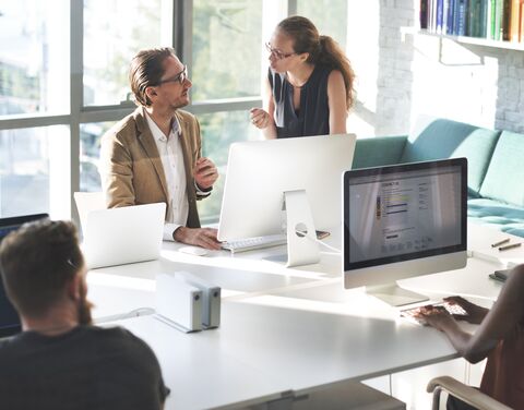 A team of five people discussing an architectural model with a laptop on the table in a modern, well-lit office.